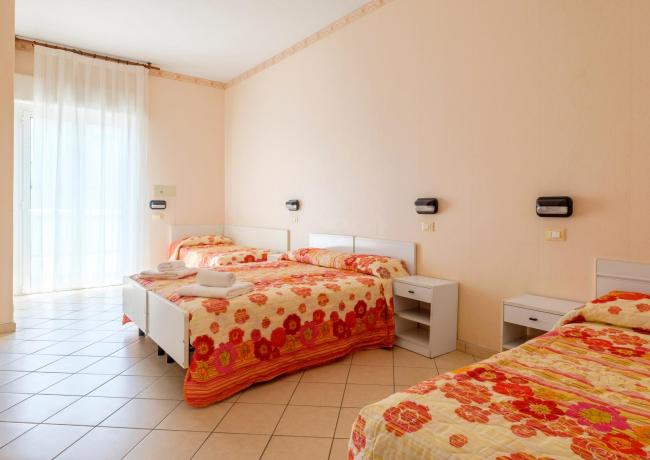 Zimmer mit drei Betten, Blumenbettdecken und natürlichem Licht.