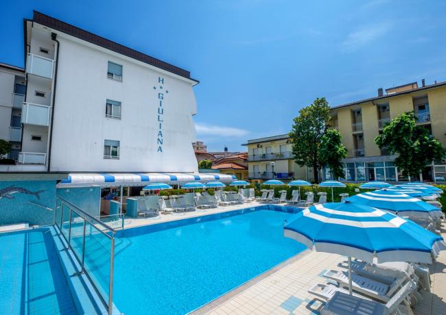 Piscina all'aperto con lettini e ombrelloni blu presso Hotel Giuliana.
