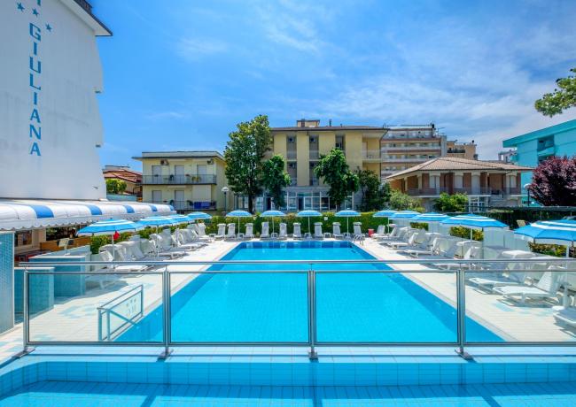 Piscina all'aperto con lettini e ombrelloni in un hotel.