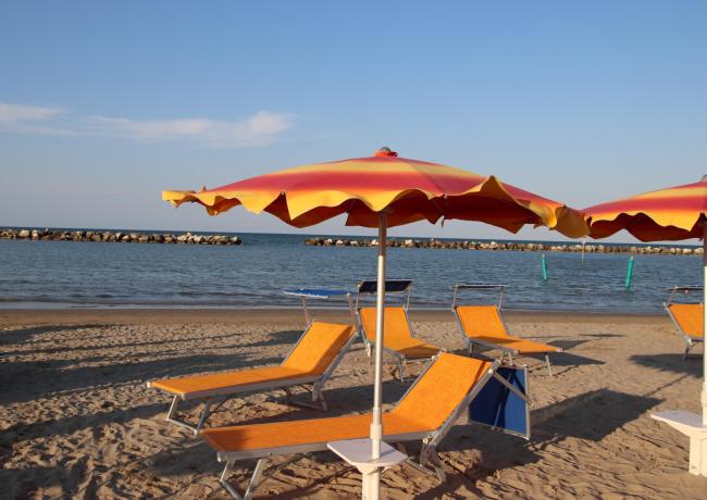 Beach with orange umbrellas and loungers, calm sea in the background.