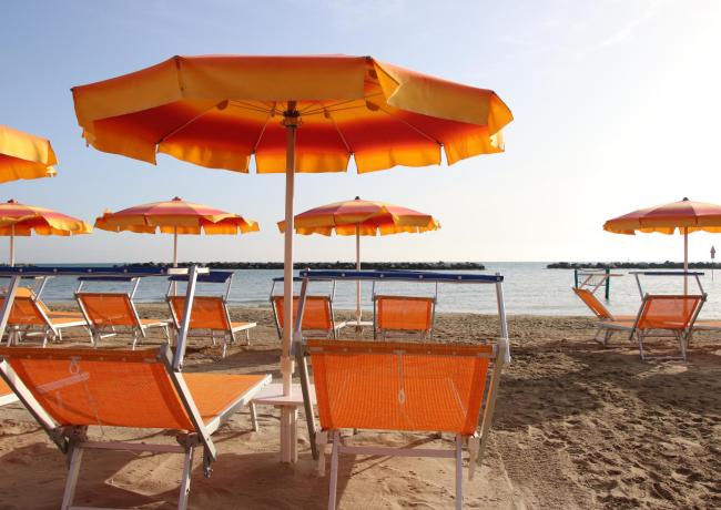 Spiaggia con ombrelloni e lettini arancioni sotto il sole.