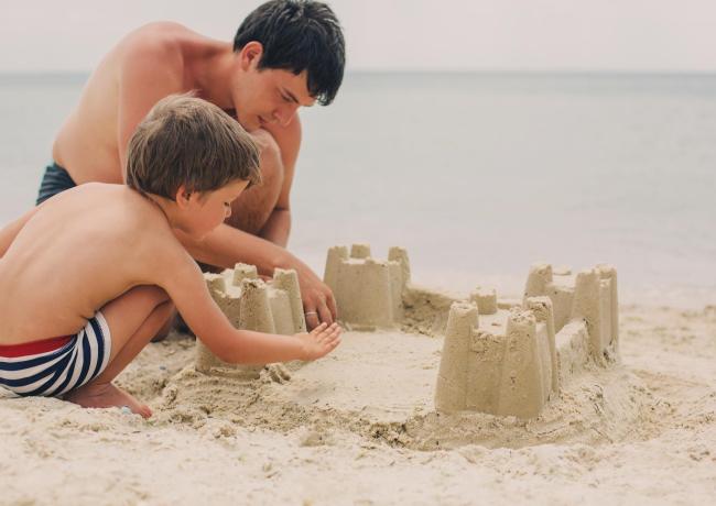 Padre e figlio costruiscono un castello di sabbia sulla spiaggia.