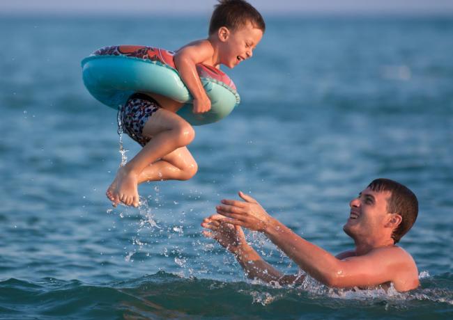 Bambino in mare con salvagente, lanciato da un adulto.