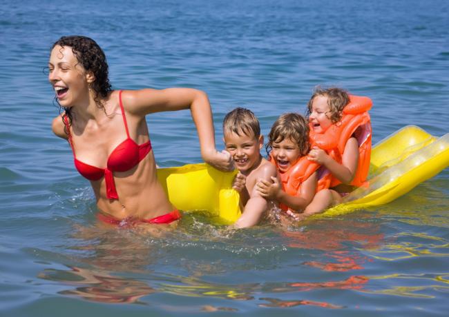 Happy woman pulls smiling kids on yellow float in the sea.