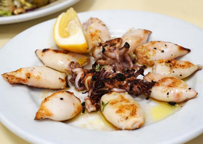 Gegrillte Calamari mit Zitrone auf einem weißen Teller.