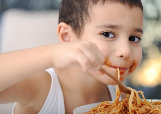 Bambino mangia spaghetti con sugo, sorriso divertente.