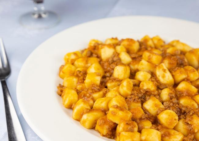 Gnocchi al ragù su piatto bianco, forchetta accanto.