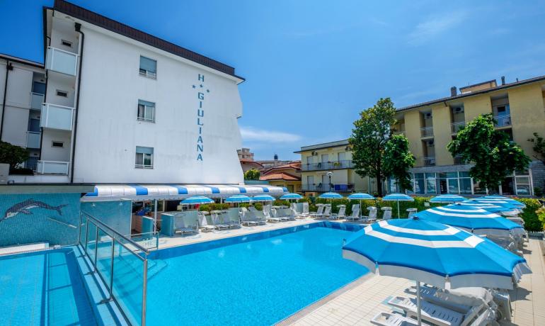Piscina all'aperto con lettini e ombrelloni blu presso Hotel Giuliana.