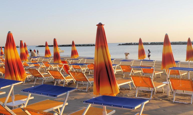 Spiaggia al tramonto con ombrelloni arancioni e mare calmo.