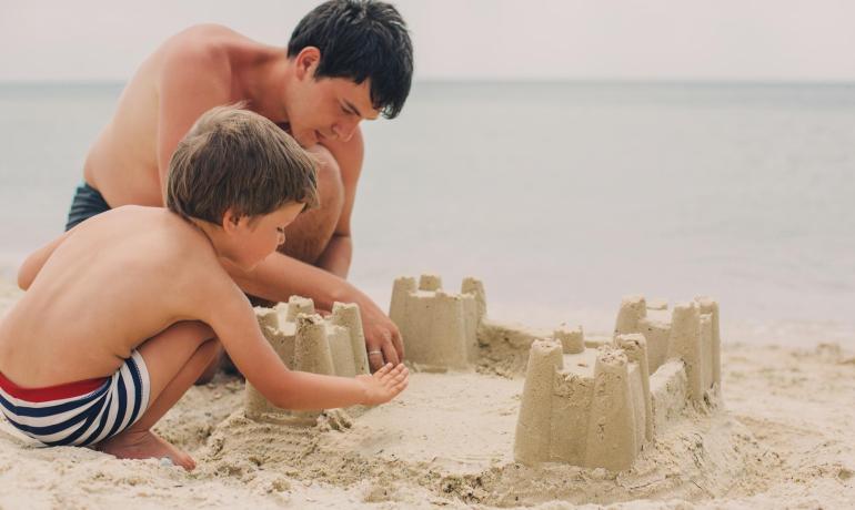 Padre e figlio costruiscono un castello di sabbia sulla spiaggia.