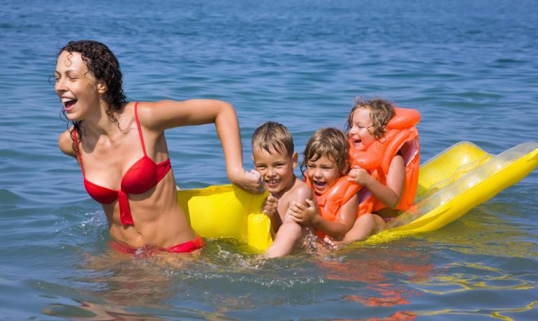 Happy woman pulls smiling kids on yellow float in the sea.