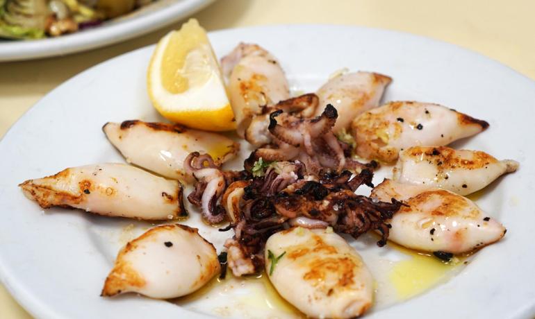 Calamari grigliati con limone su un piatto bianco.