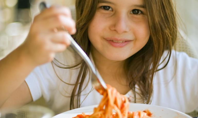 Bambina mangia spaghetti al sugo con un sorriso.