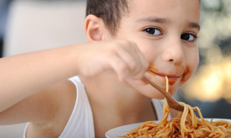 Bambino mangia spaghetti con sugo, sorriso divertente.