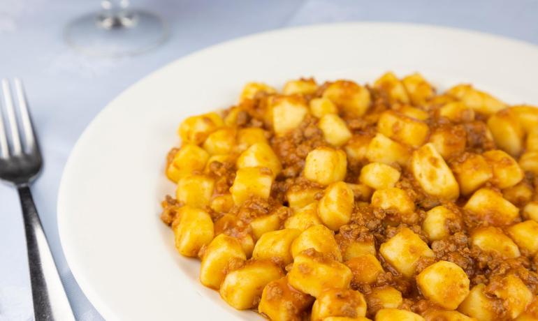 Gnocchi al ragù su piatto bianco, forchetta accanto.
