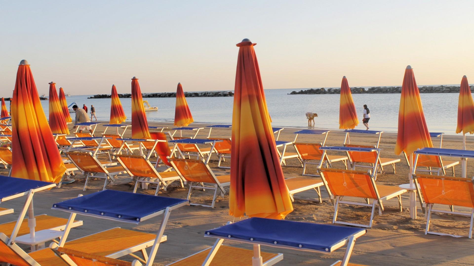 Spiaggia al tramonto, ombrelloni arancioni chiusi e mare calmo, atmosfera serena e rilassante.
