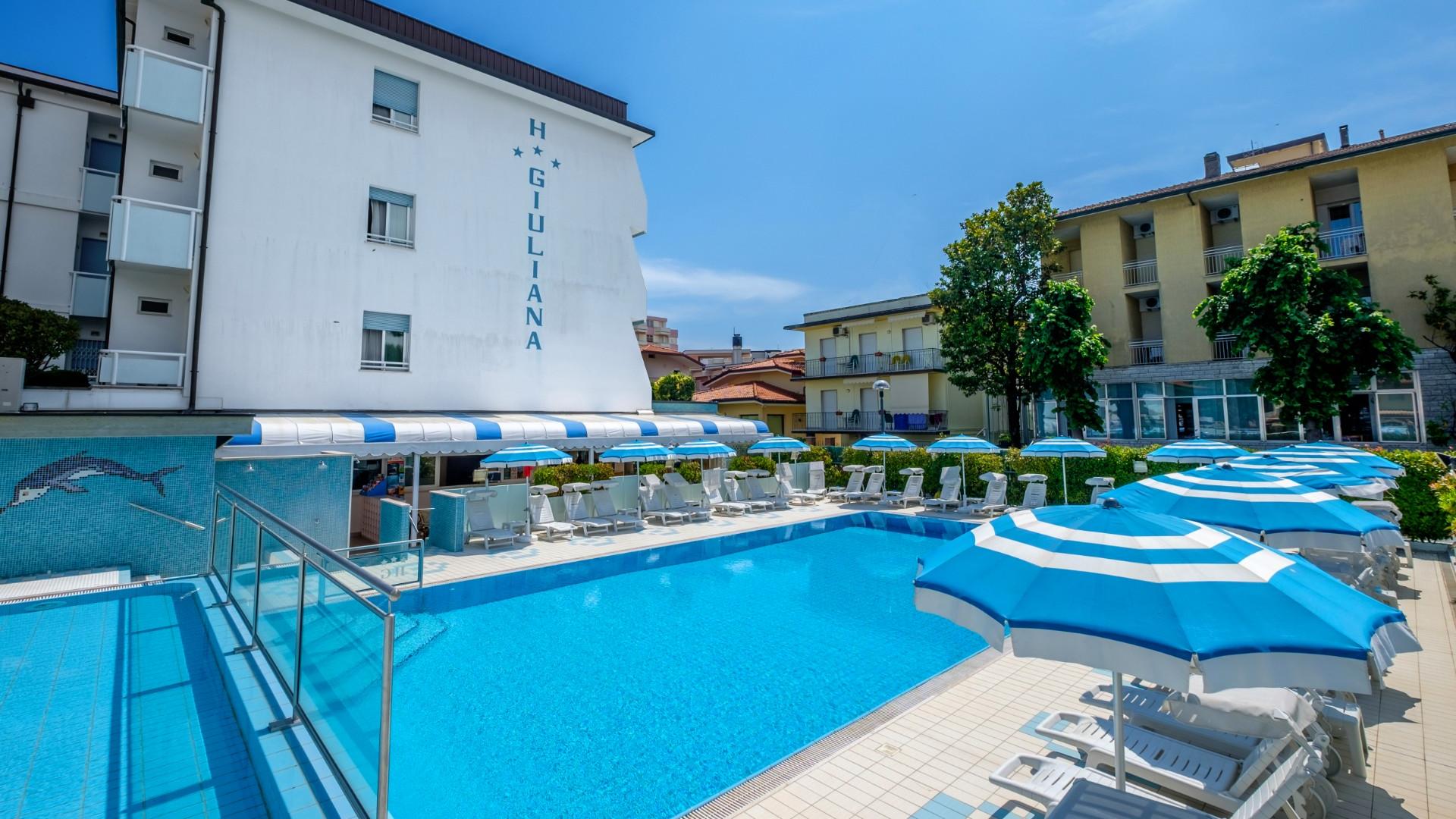 Piscina azzurra con ombrelloni bianchi e blu, atmosfera estiva e rilassante.