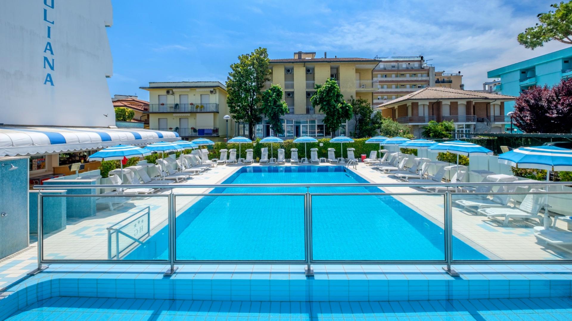 Piscina soleggiata con lettini e ombrelloni blu, atmosfera rilassante e vacanziera.