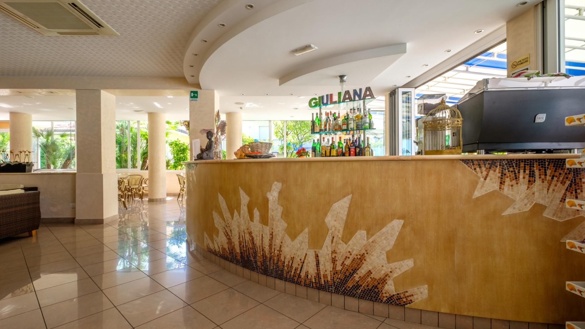 Elegante bar con bancone decorato, atmosfera luminosa e accogliente, bottiglie colorate in esposizione.