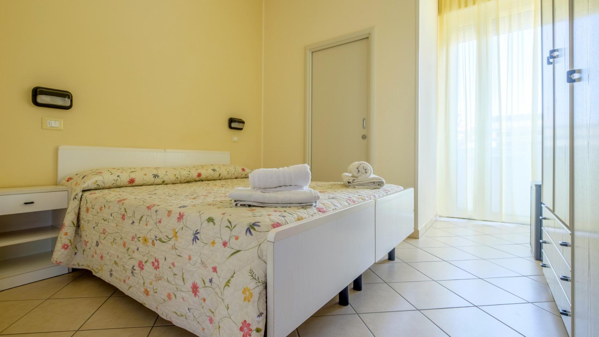 Camera luminosa, accogliente, con letto floreale e asciugamani, trasmette serenità e calore.