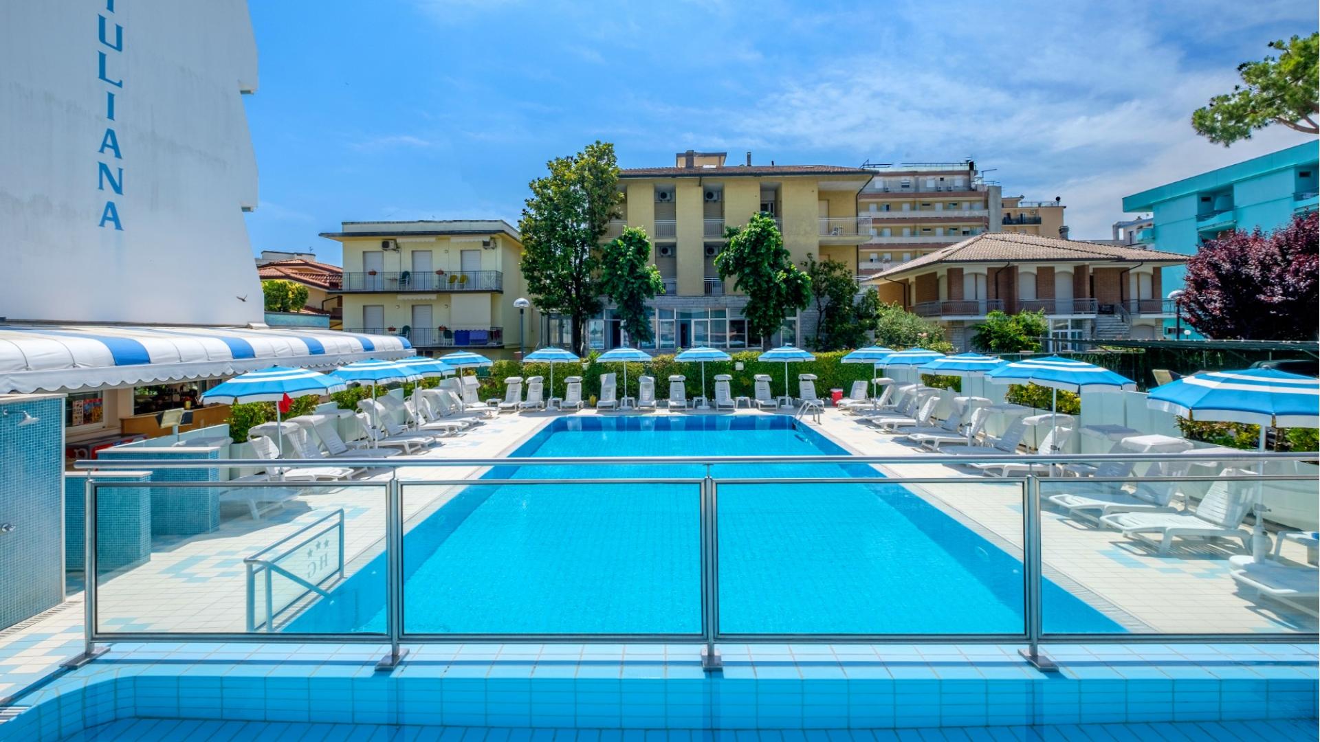 Piscina azzurra con lettini e ombrelloni, atmosfera estiva e rilassante.