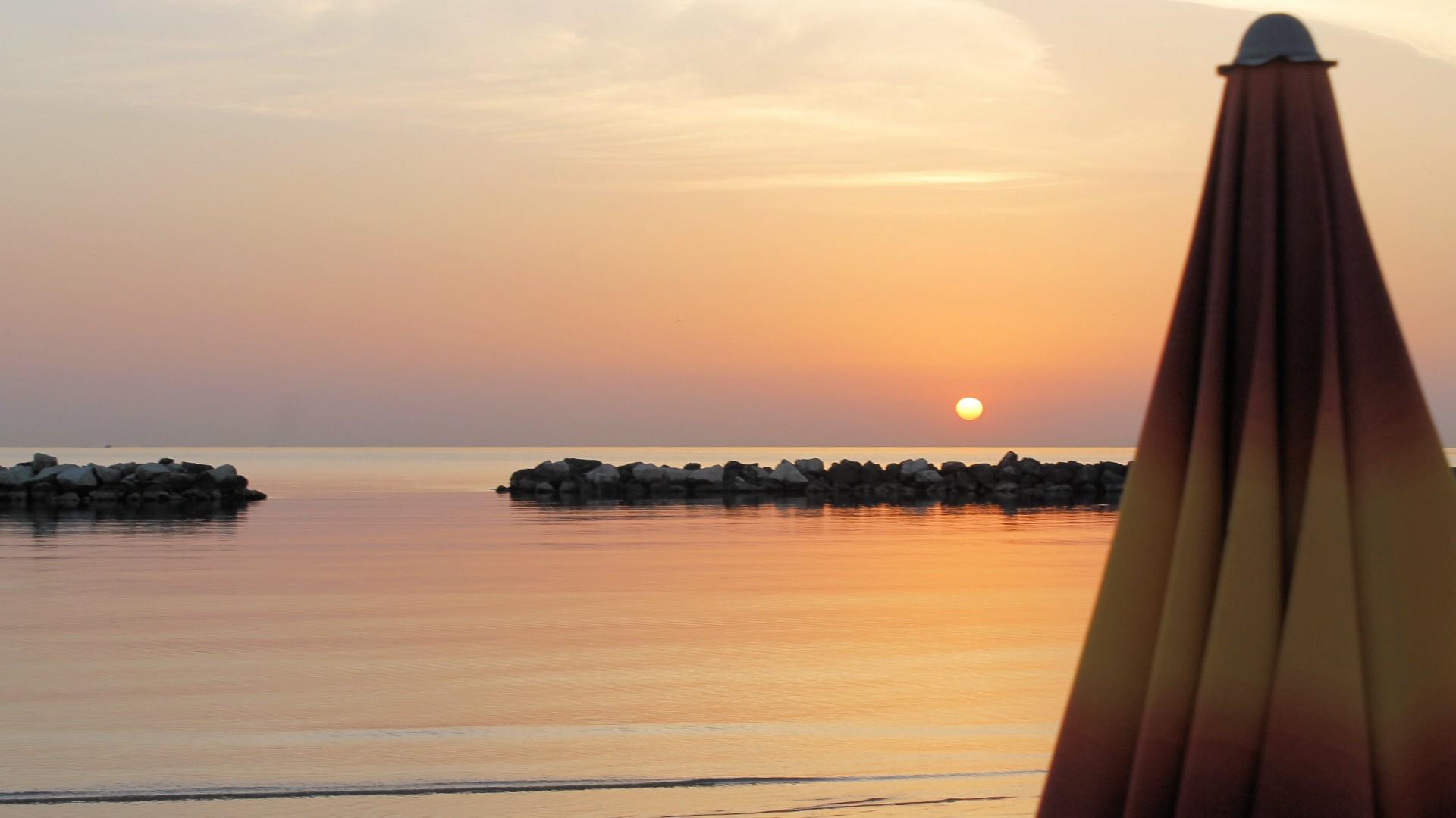 Tramonto sereno sul mare calmo, ombrellone chiuso, atmosfera di pace e bellezza naturale.