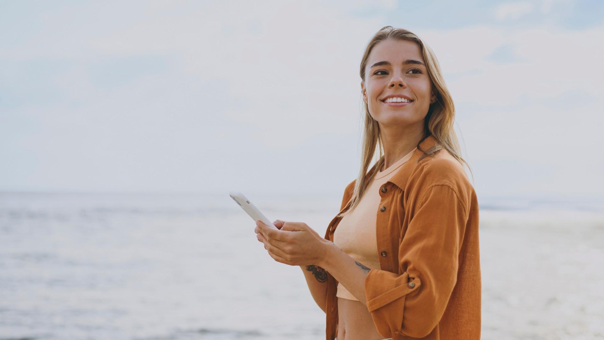 Donna sorridente al mare con cellulare, atmosfera serena e rilassata.