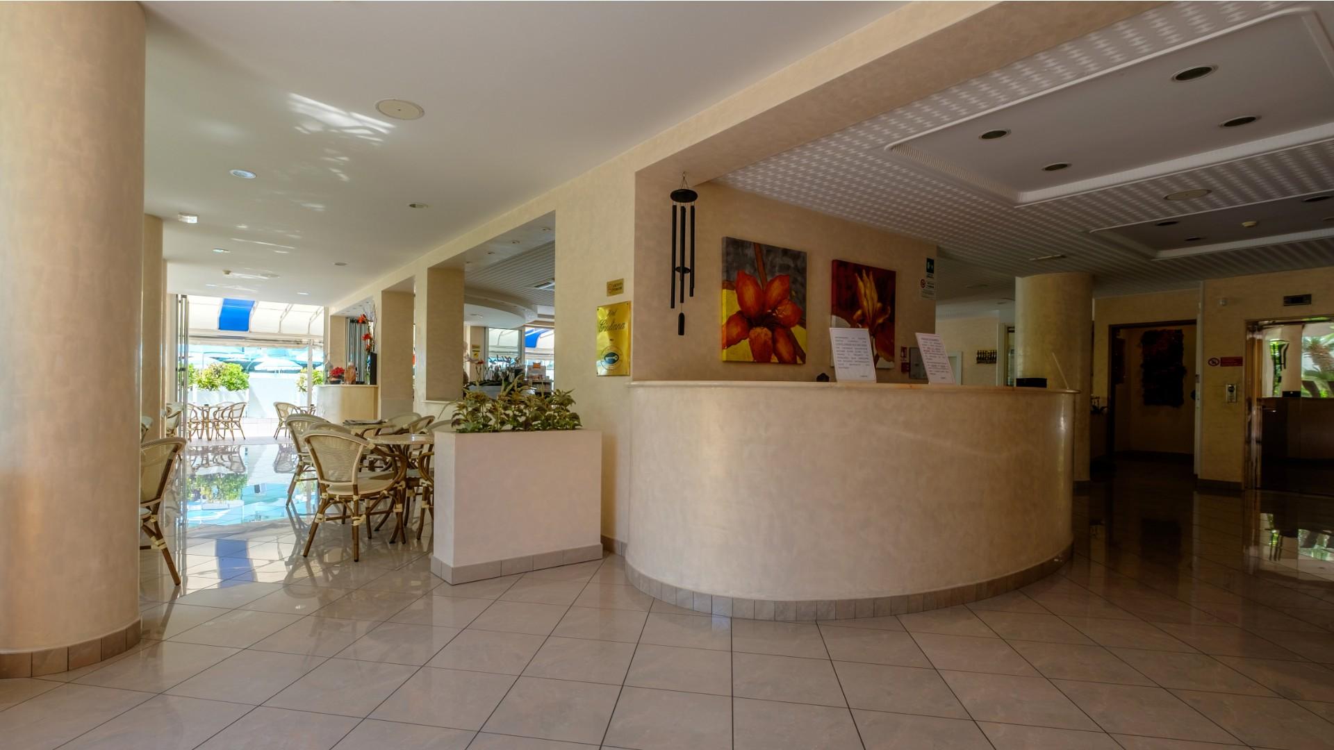 Hall luminosa con arredi eleganti, piante e quadri colorati, atmosfera accogliente e rilassante.