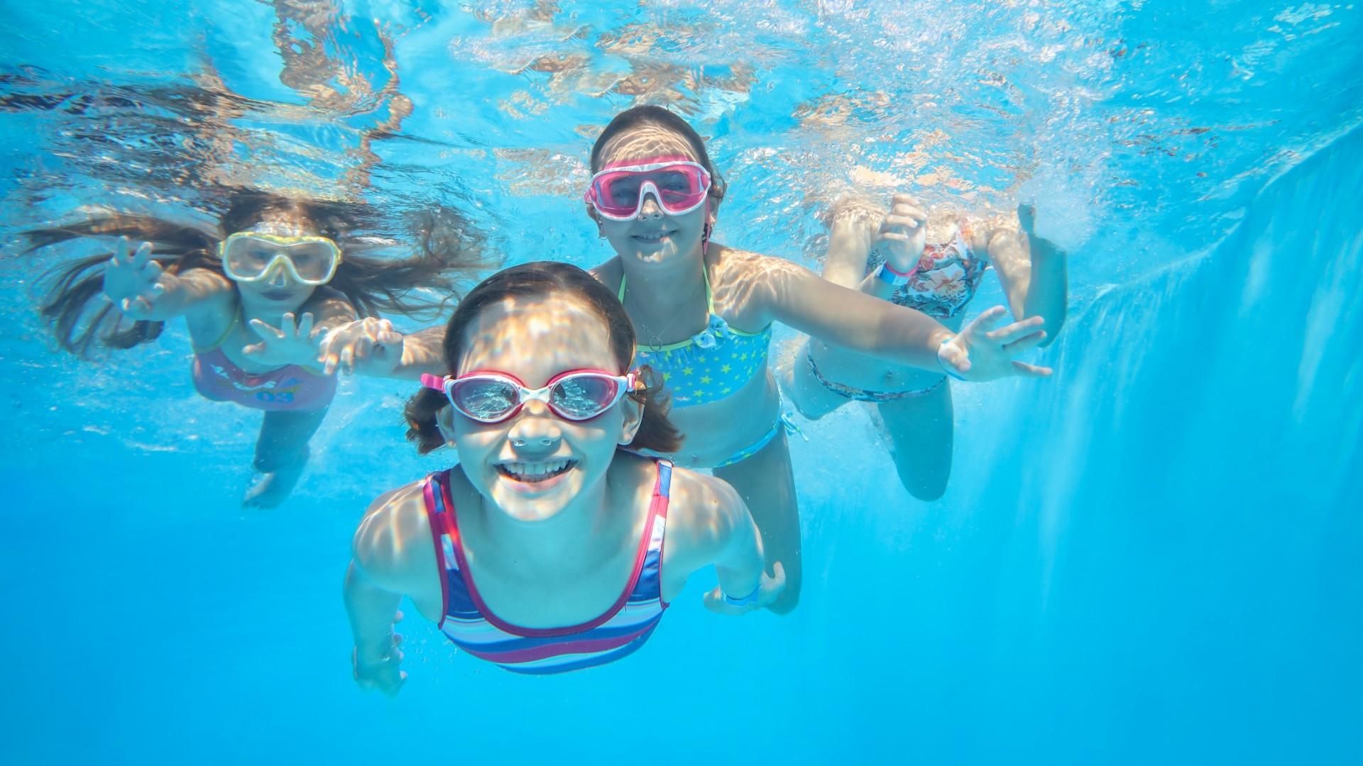 Bambini felici nuotano sott'acqua, sorridenti e pieni di gioia, indossando occhialini colorati.