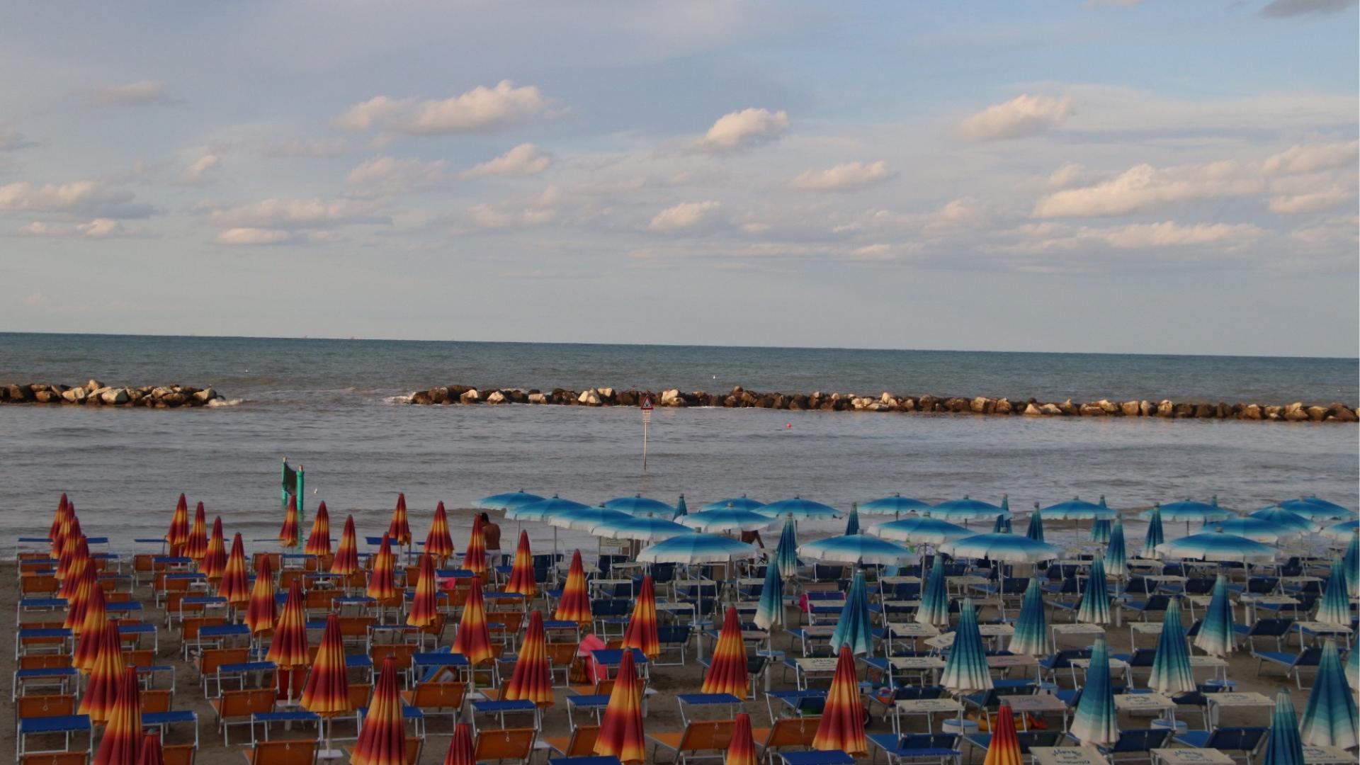 Spiaggia deserta, ombrelloni colorati chiusi, mare calmo e cielo sereno al tramonto.