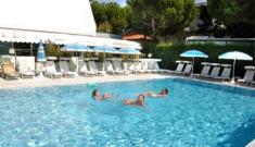 Piscina soleggiata, persone rilassate, ombrelloni azzurri, atmosfera estiva e serena.