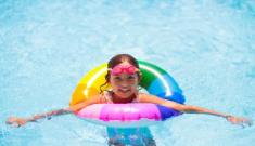 Bambina felice in piscina con ciambella colorata, sprigiona gioia e spensieratezza estiva.