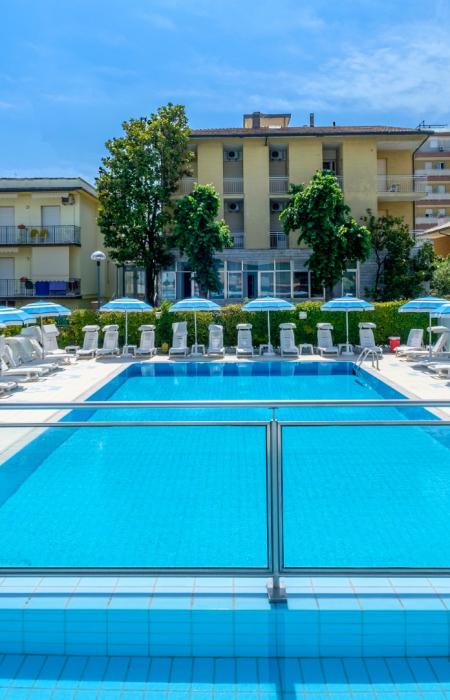 Piscina soleggiata con lettini e ombrelloni blu, atmosfera rilassante e vacanziera.