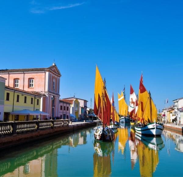 Barche colorate su canale, case pastello, cielo limpido: un giorno sereno e pittoresco.