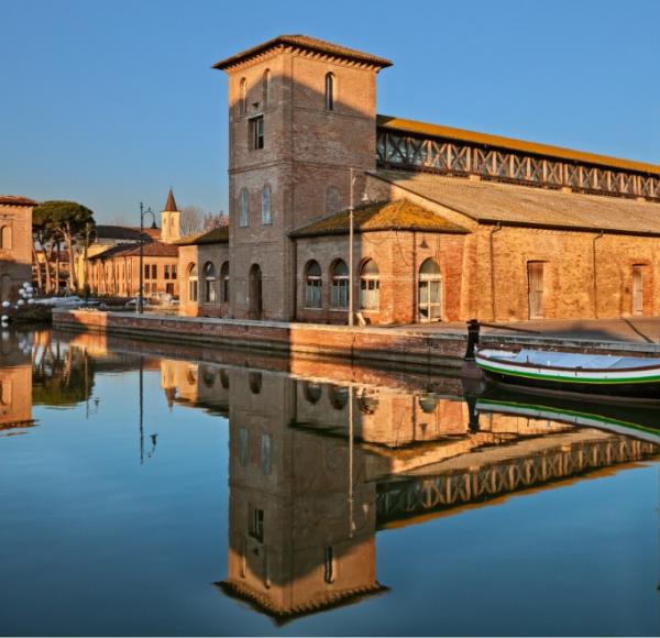 Tranquillo canale riflette antichi edifici di mattoni al tramonto, atmosfera serena e storica.