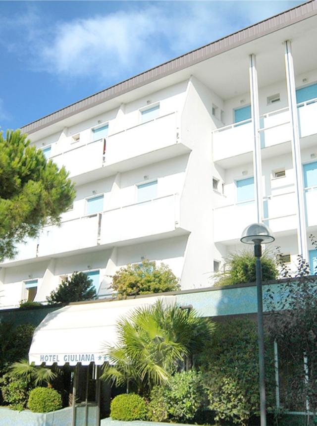 Hotel bianco, cielo azzurro, vegetazione rigogliosa; atmosfera serena e accogliente.