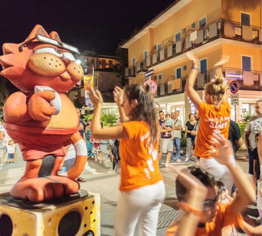 Festa notturna vivace, persone ballano con una mascotte di gatto arancione gigante.
