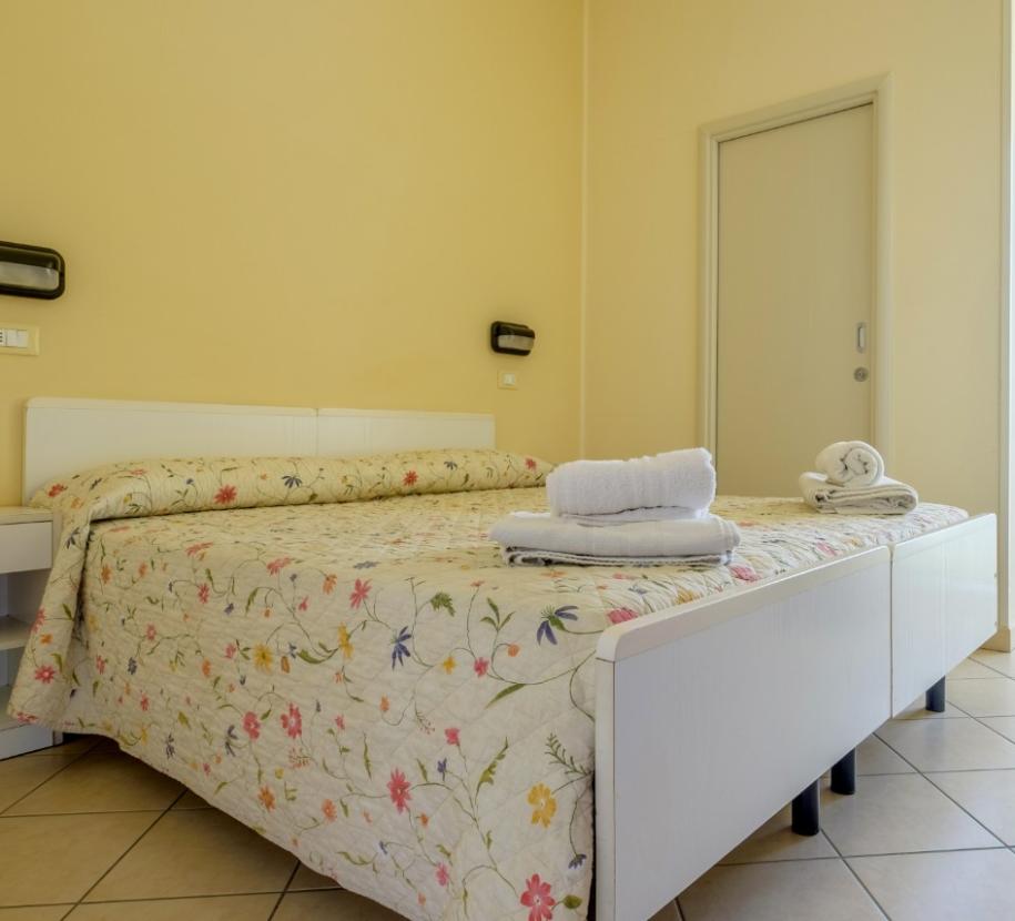 Camera luminosa con letto matrimoniale, copriletto floreale e asciugamani ordinati.