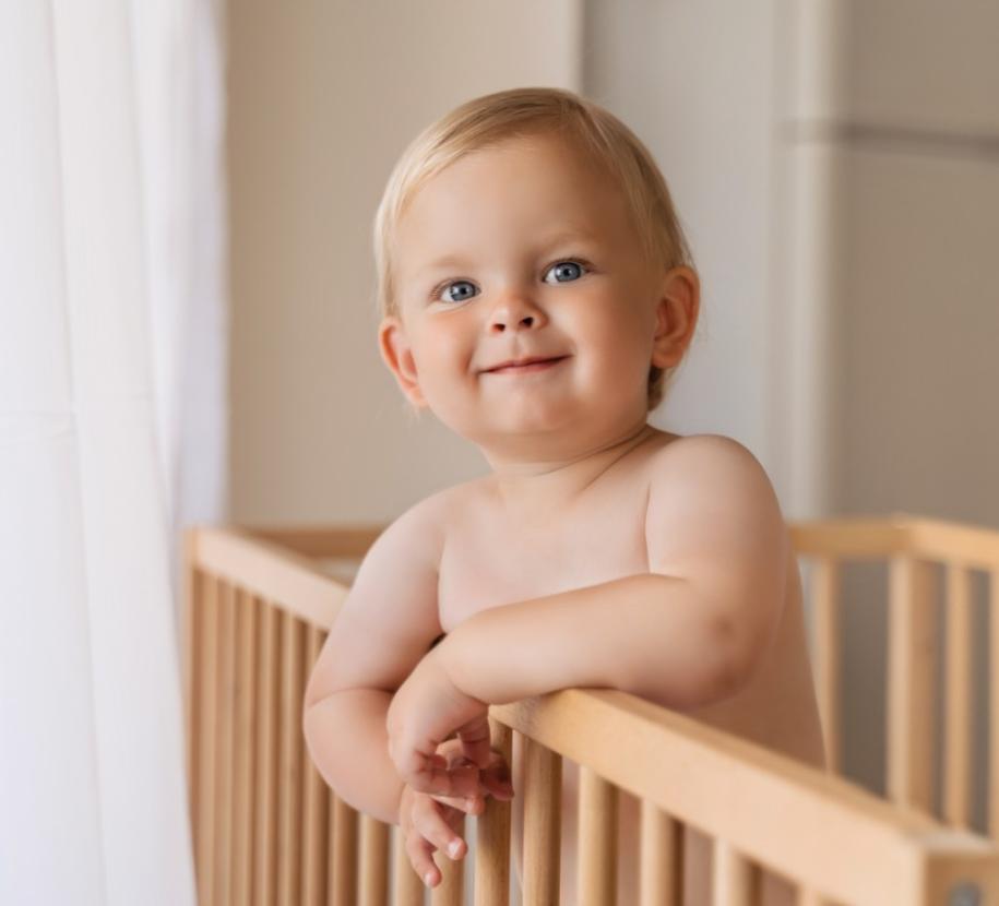 Bambino felice in culla di legno, sorriso dolce, luce soffusa, atmosfera serena.