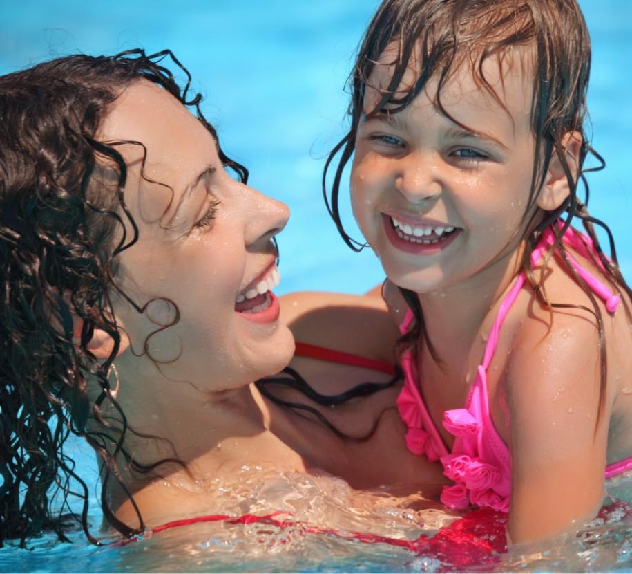 Madre e figlia ridono felici in piscina, godendo di un momento di gioia estiva.