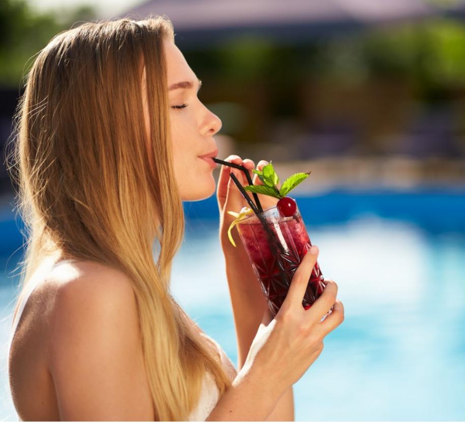 Donna rilassata beve cocktail estivo a bordo piscina, godendo il sole.